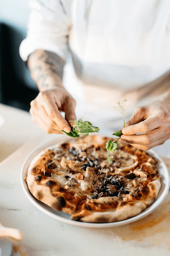 Chef topping a pizza with spinach.